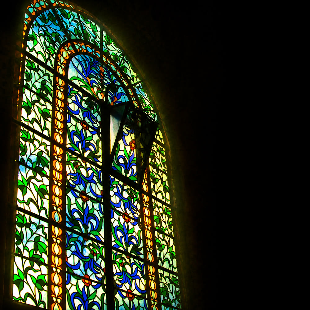 An arched stained-glass window with a floral leaded-glass pattern — the windows of the synagogue.
